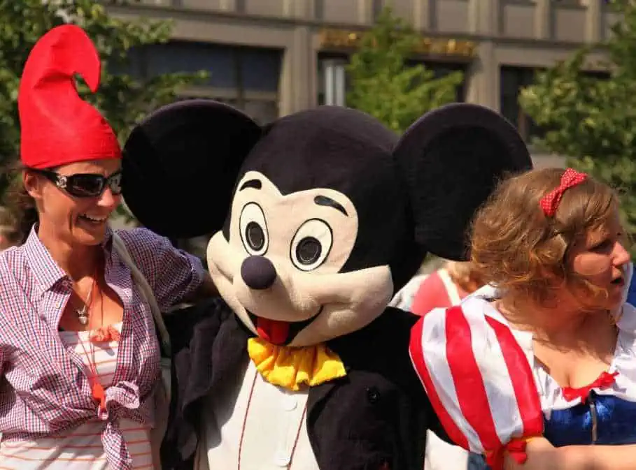 A Women taking picture with Micky Mouse While wearing Sunglasses on a Sunny Day