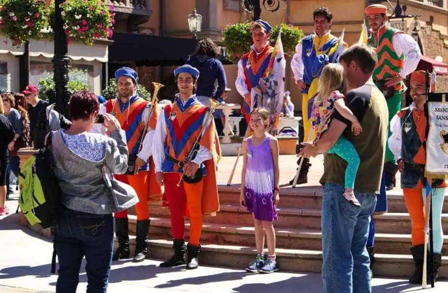 A family in Comfortable Clothing taking pictures with entertainers from Italy at Disney World on a Sunny Day.